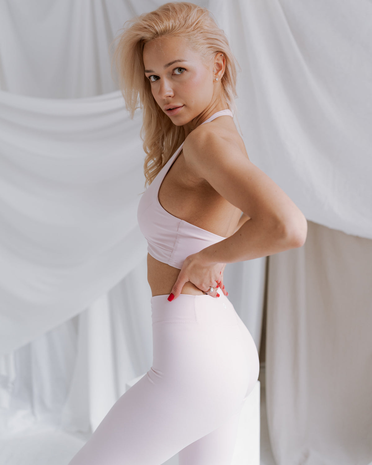 Woman wearing a white sports bra and leggings against a white draped background