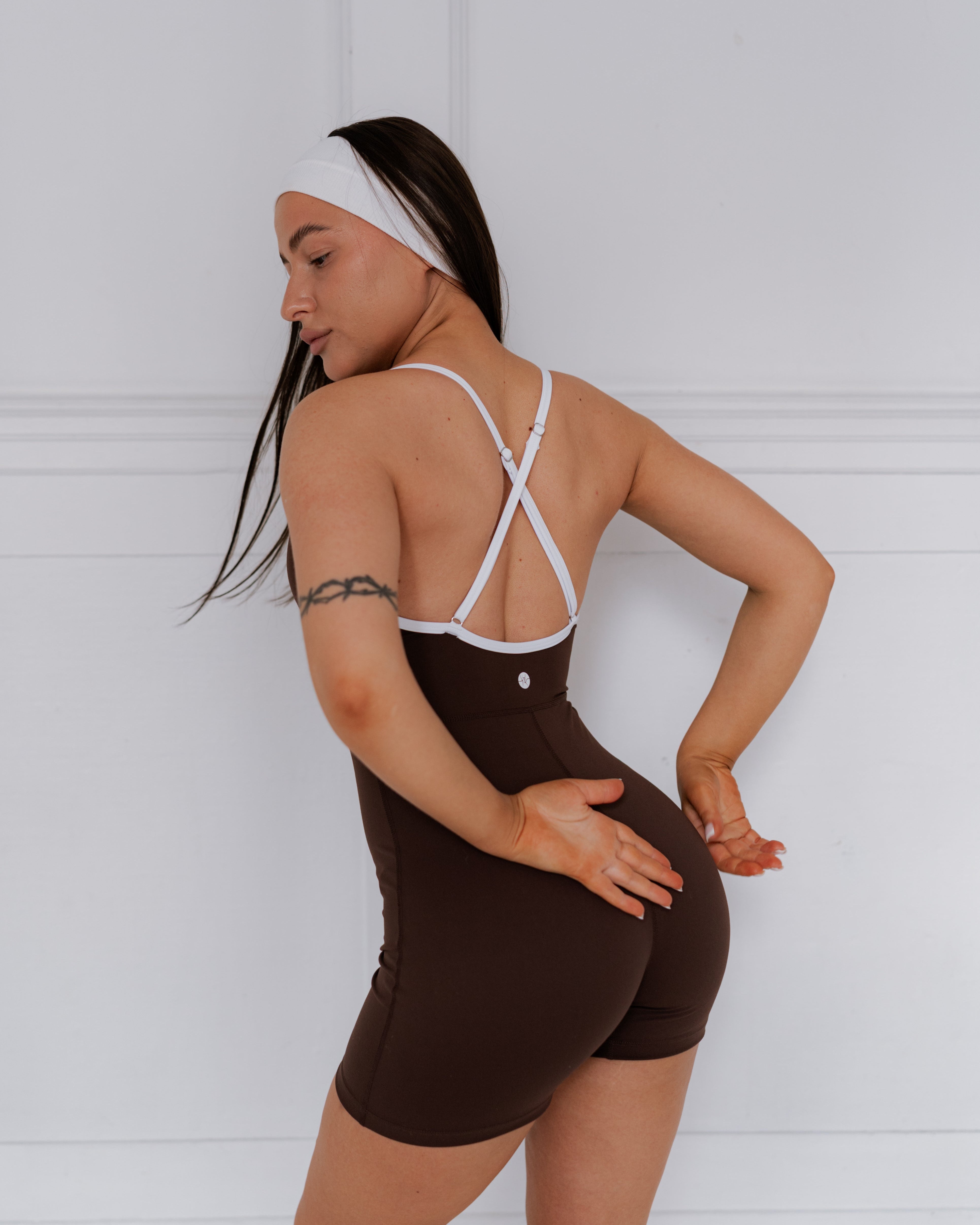 Woman wearing a brown bodysuit with white straps against a white background
