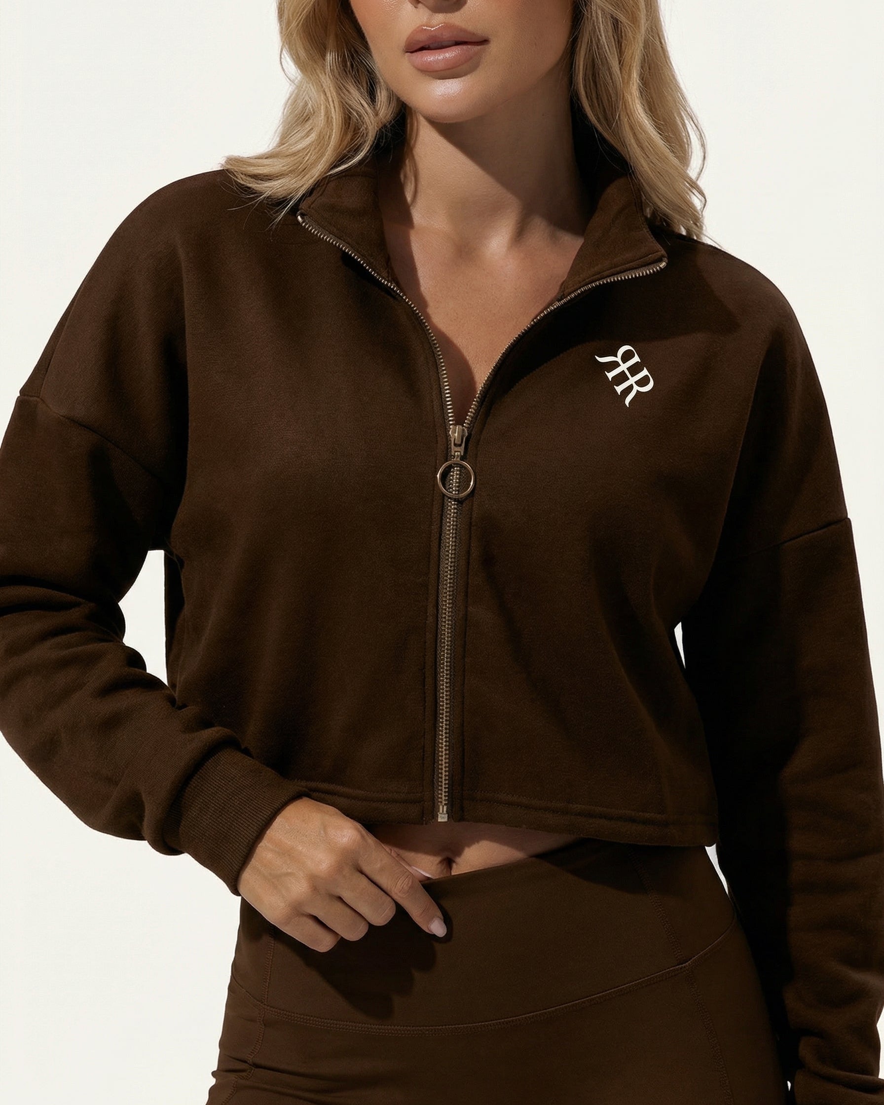 Woman wearing a brown zip-up sweatshirt with a logo on a white background