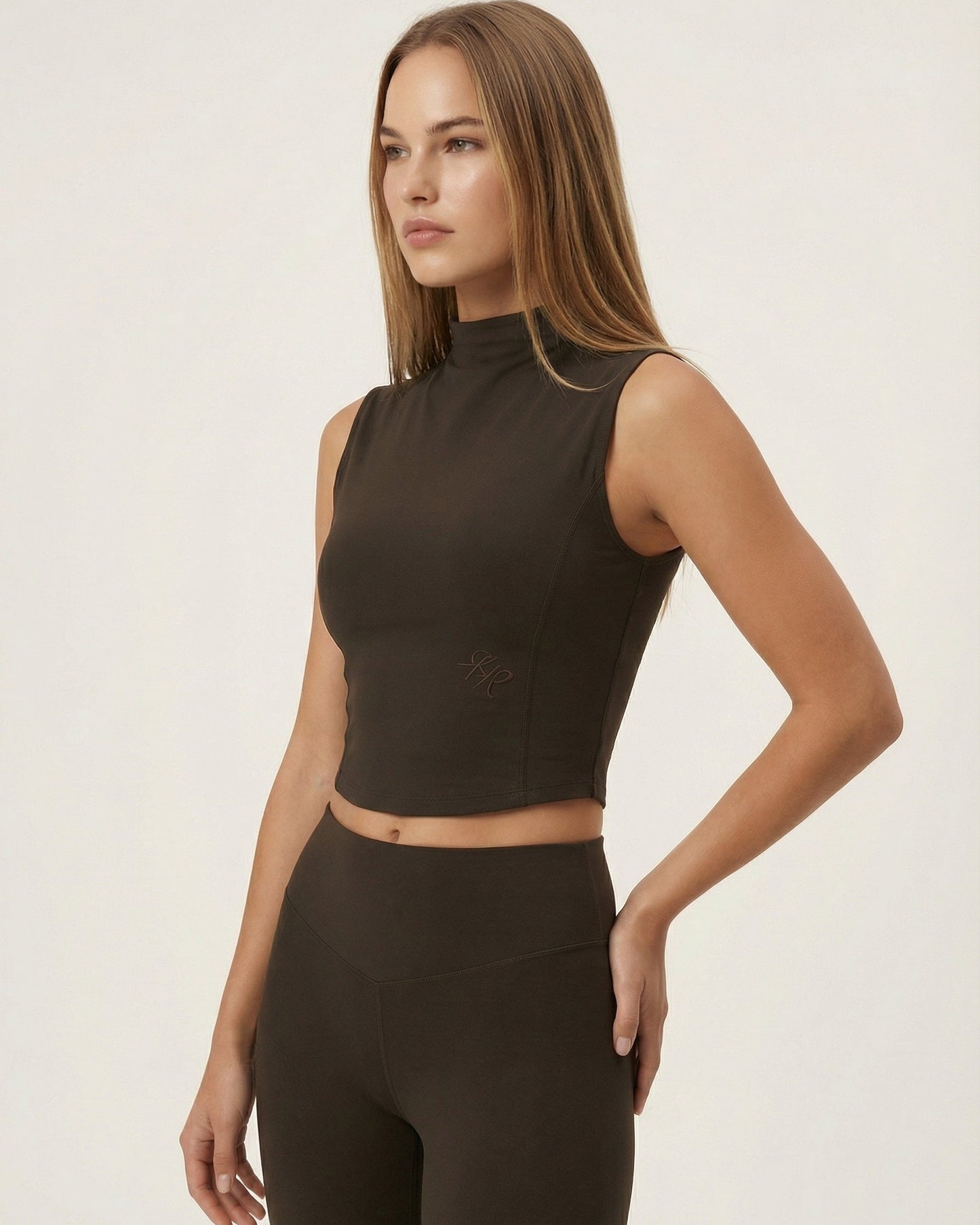 Woman wearing a brown sleeveless top and high-waisted leggings on a white background