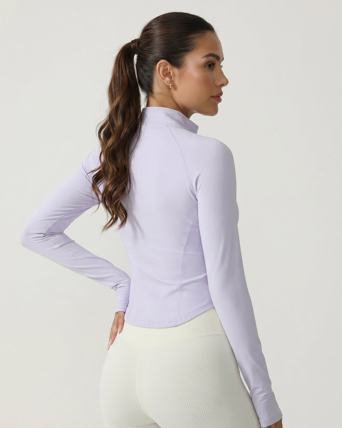 Woman wearing a light purple long-sleeve athletic top and white leggings on a plain background