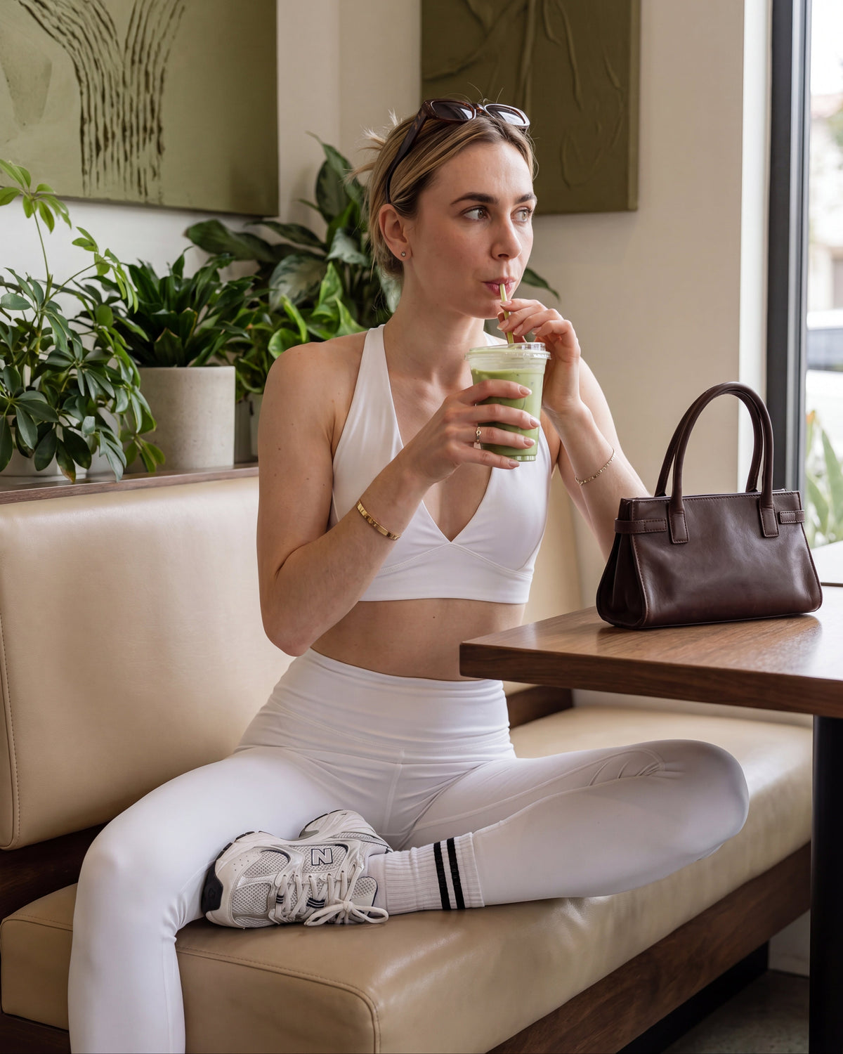Woman in athletic wear drinking a green smoothie in a cafe.