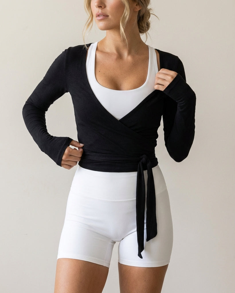 Woman wearing a black long-sleeve top with a white square neckline and white shorts on a plain background