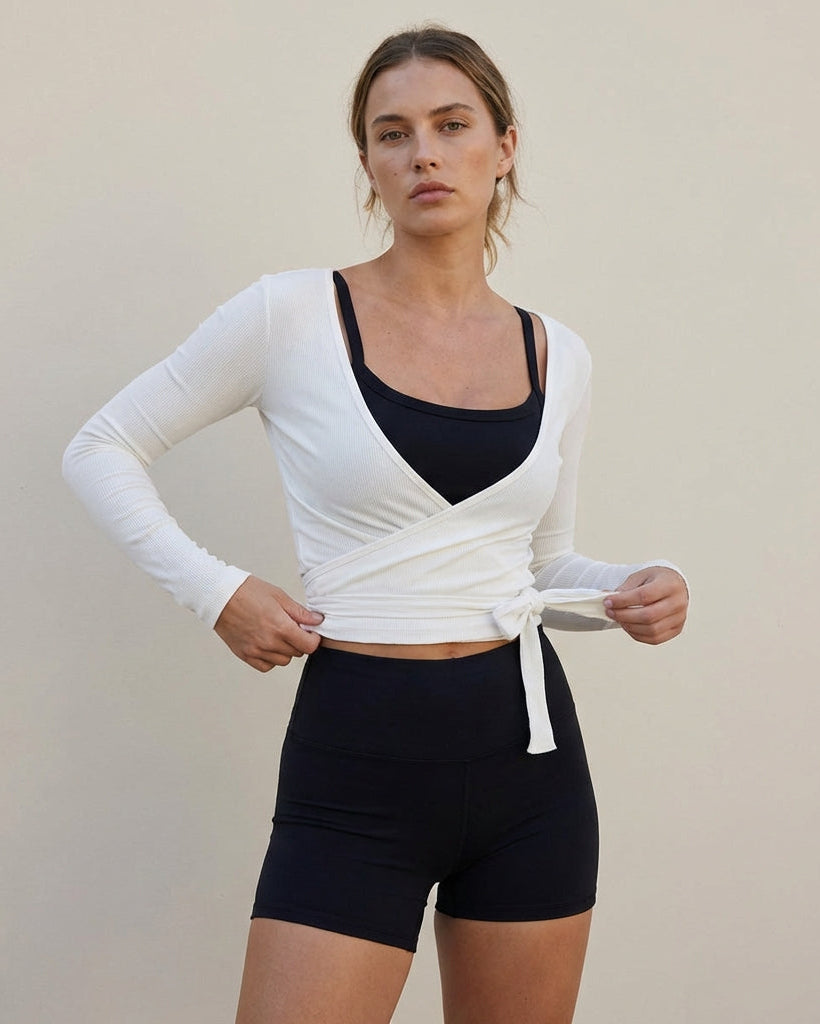 Woman wearing a white long-sleeve top and black shorts against a beige background