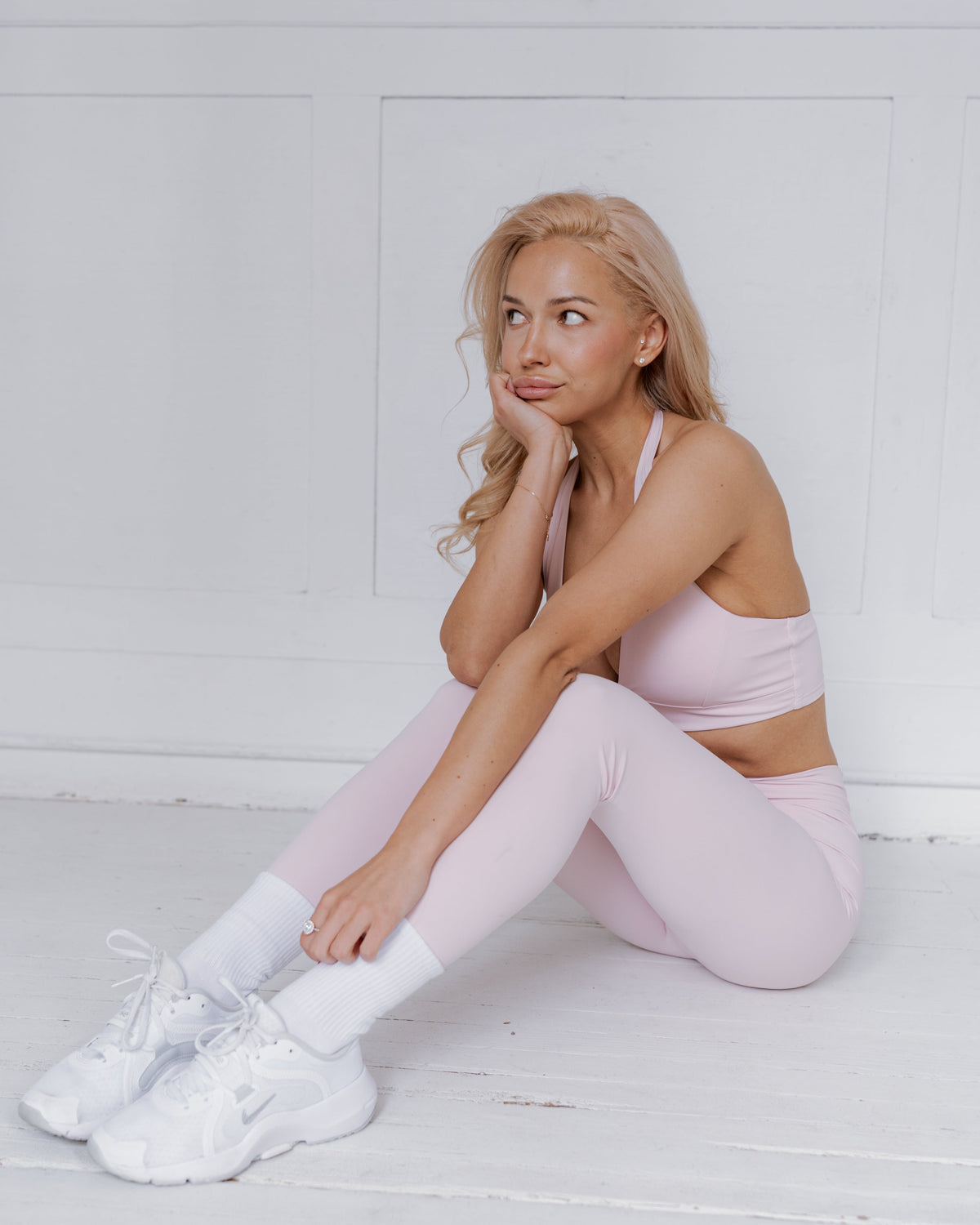 Woman in pink athletic wear sitting on a white floor.