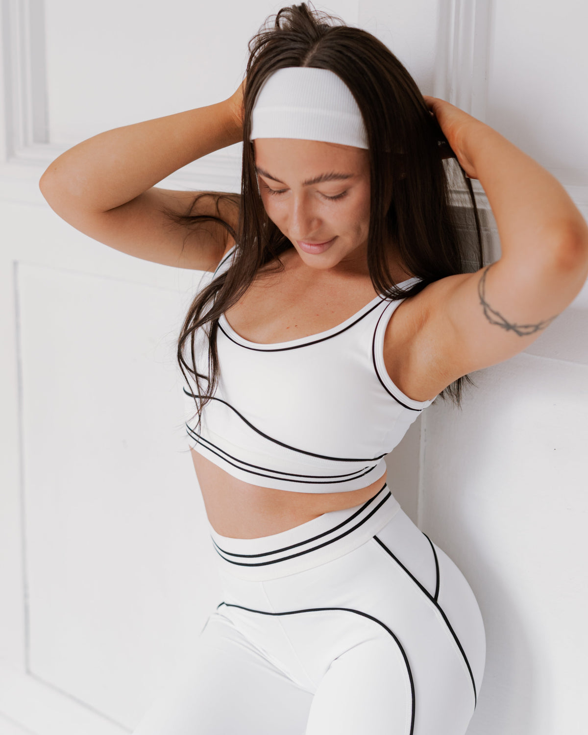 Woman wearing a white and black athletic outfit with a headband against a light background