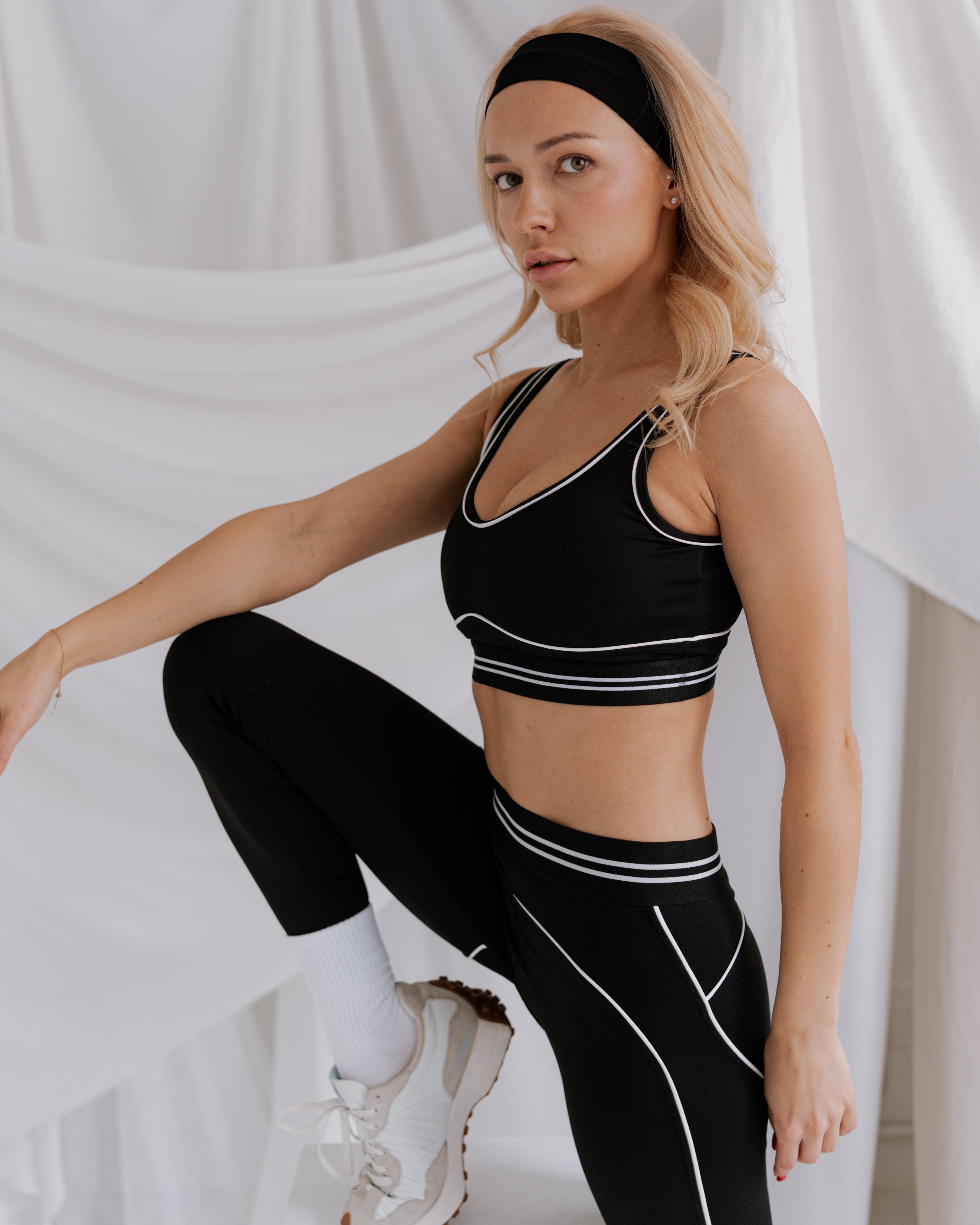 Woman wearing a black sports bra and leggings with white accents against a white background