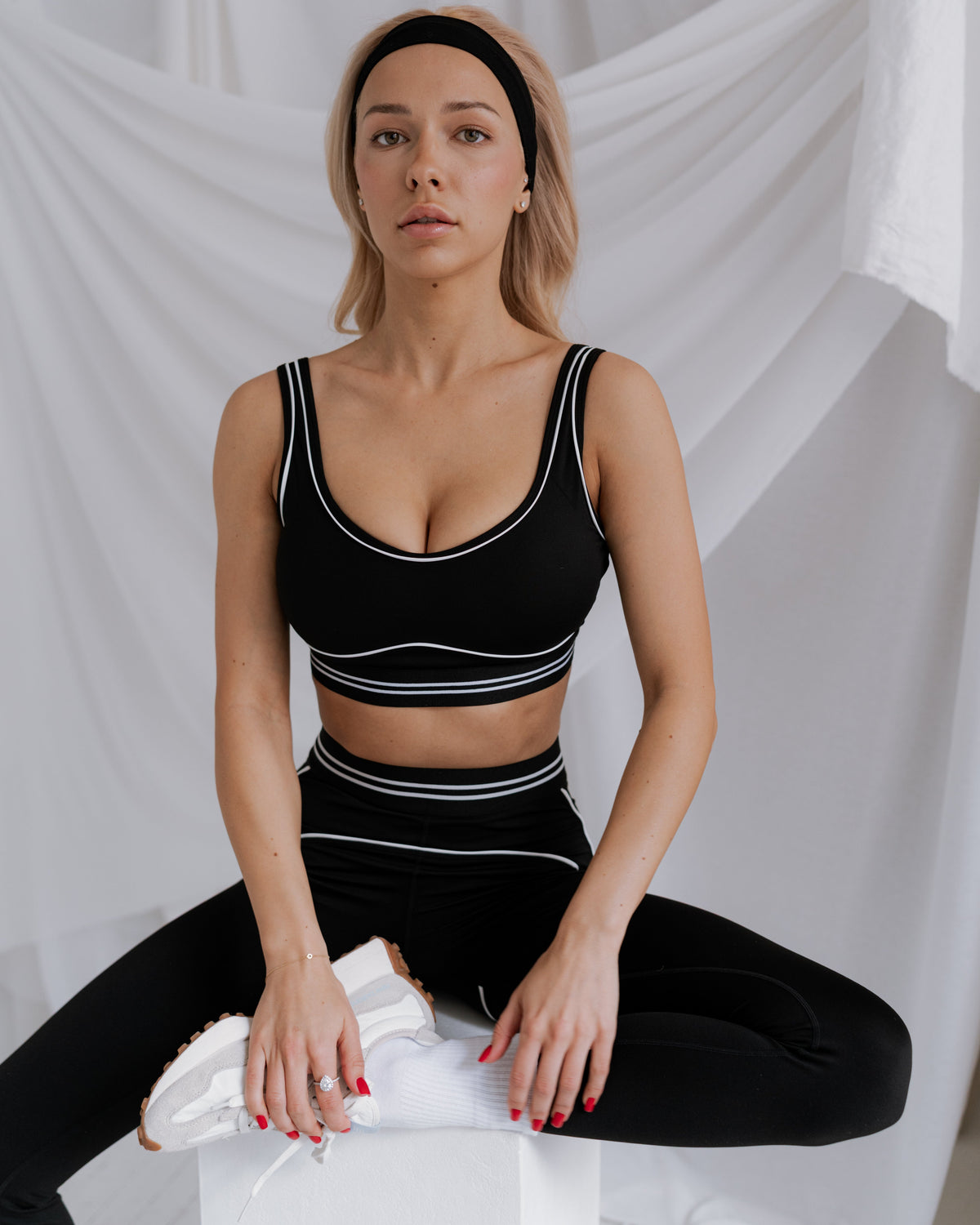 Woman in black athletic wear sitting on a white surface with a white curtain background