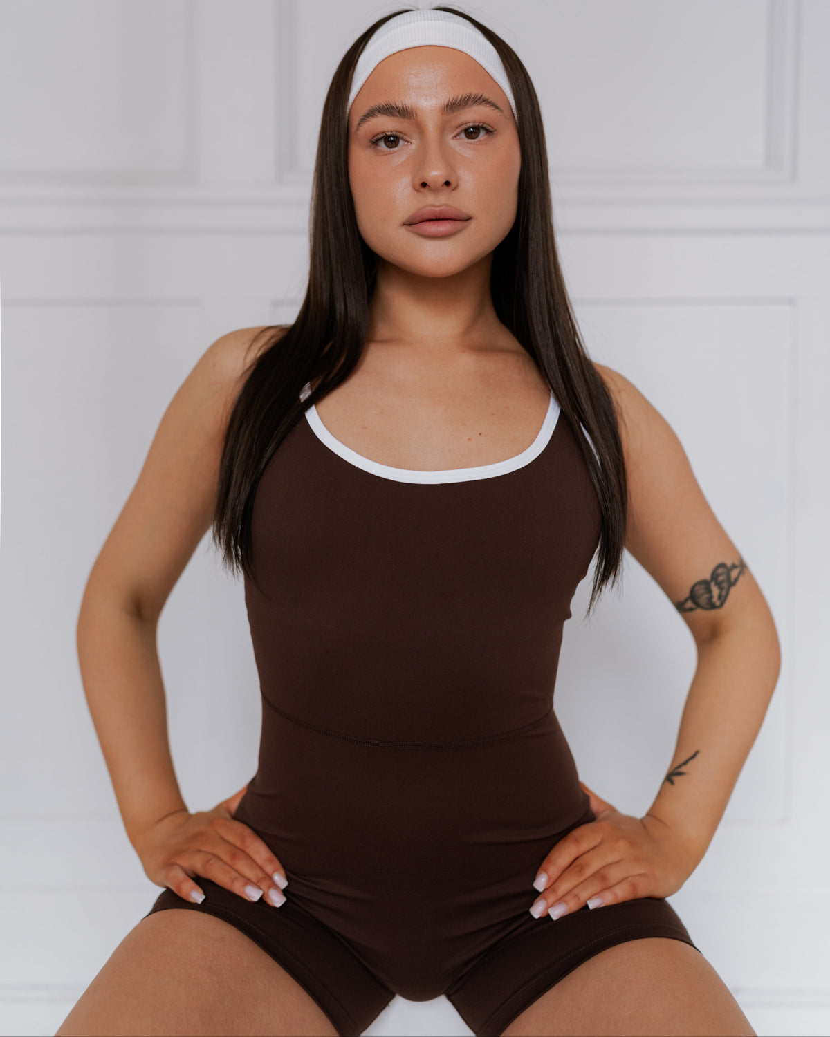 Woman wearing a brown romper with a white headband against a white background
