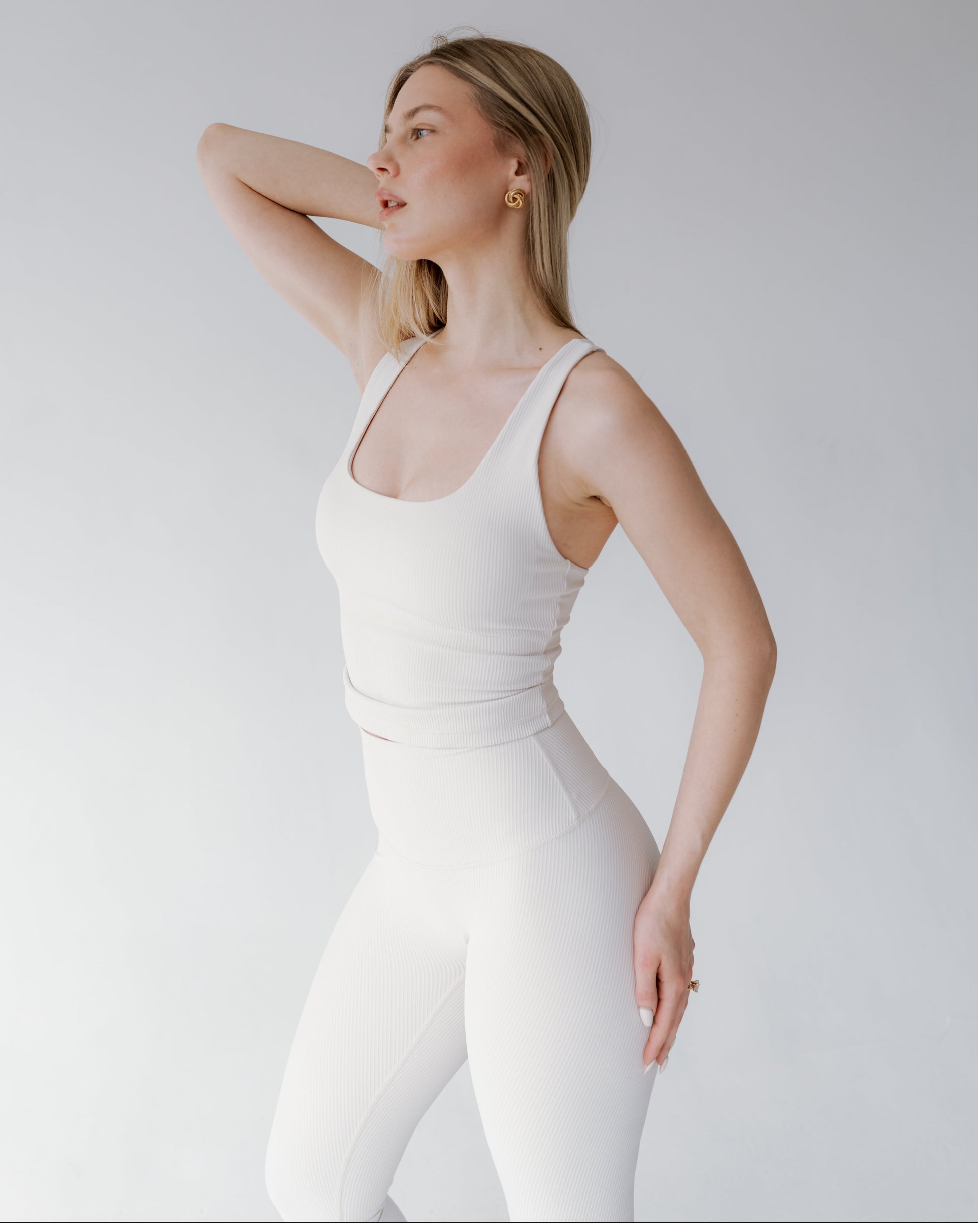 Woman wearing a white sleeveless top and leggings against a plain background