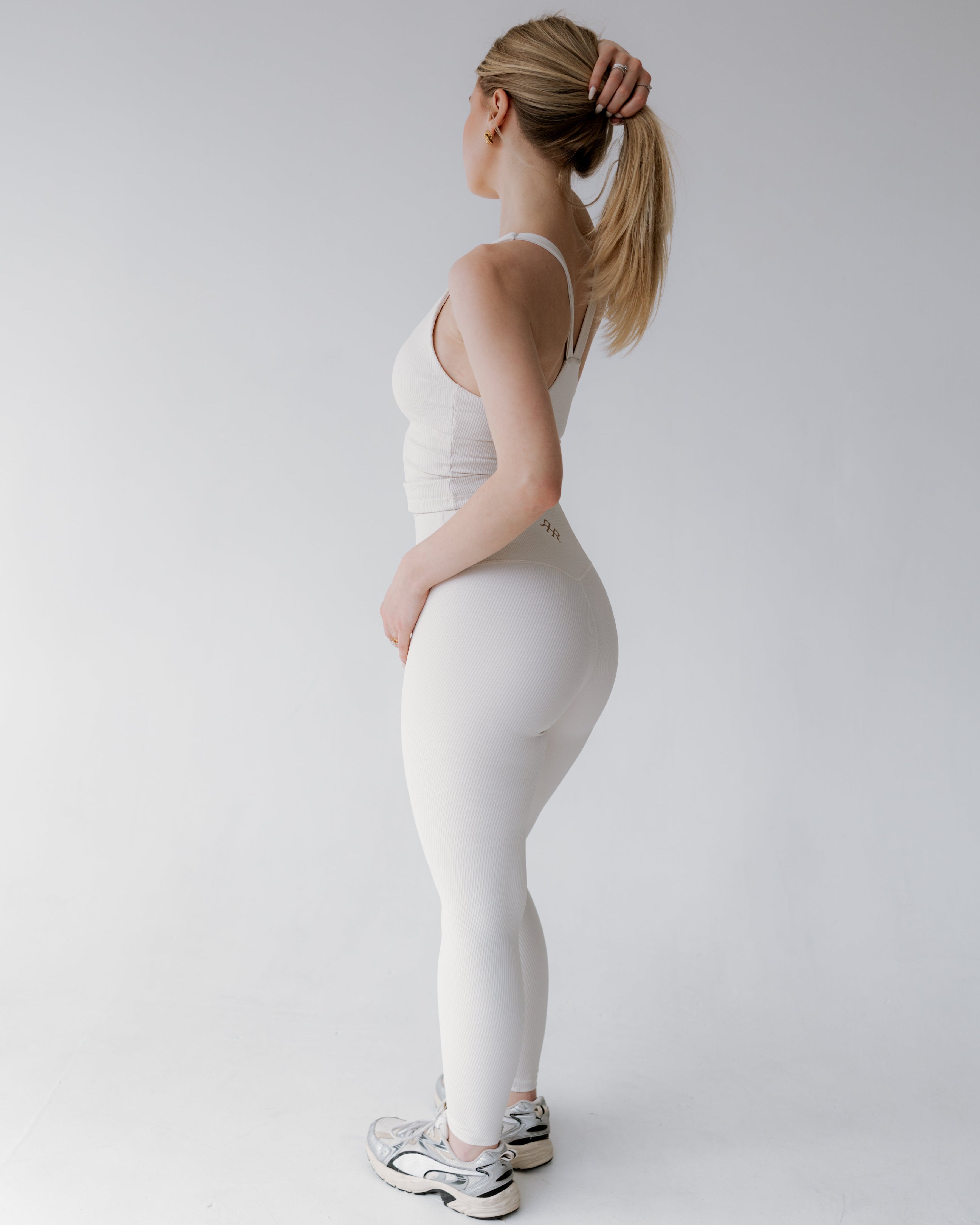 Person wearing a white tank top and leggings on a plain background