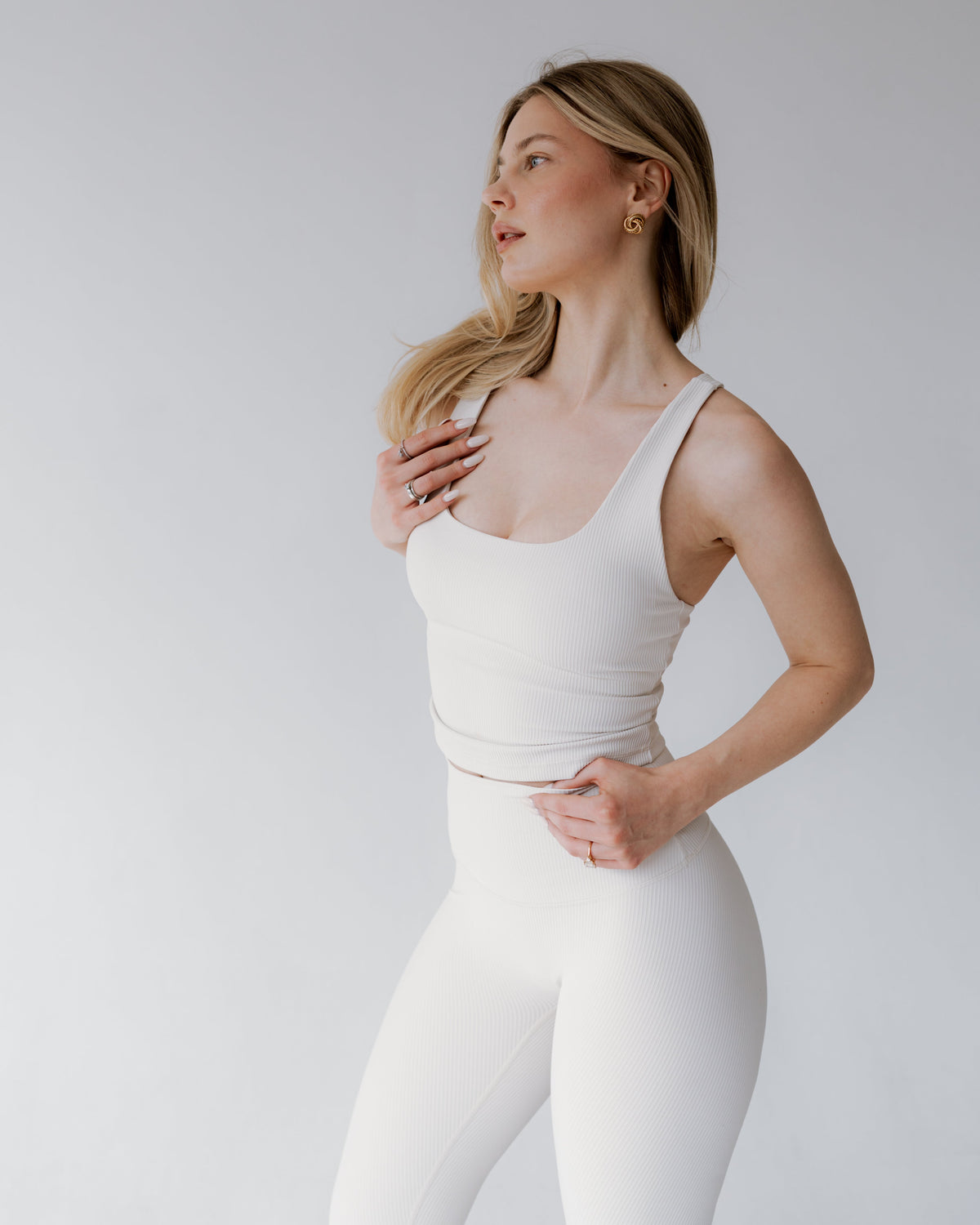 Woman wearing a white tank top and leggings against a plain background