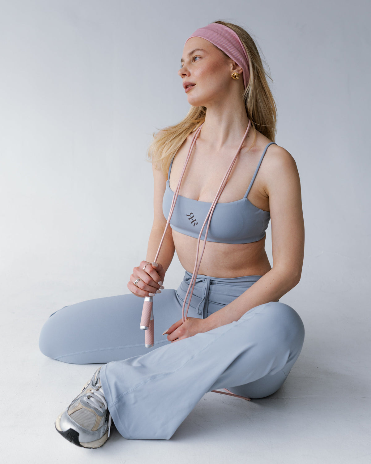 Woman in light blue athletic wear sitting on the floor with a pink resistance band.