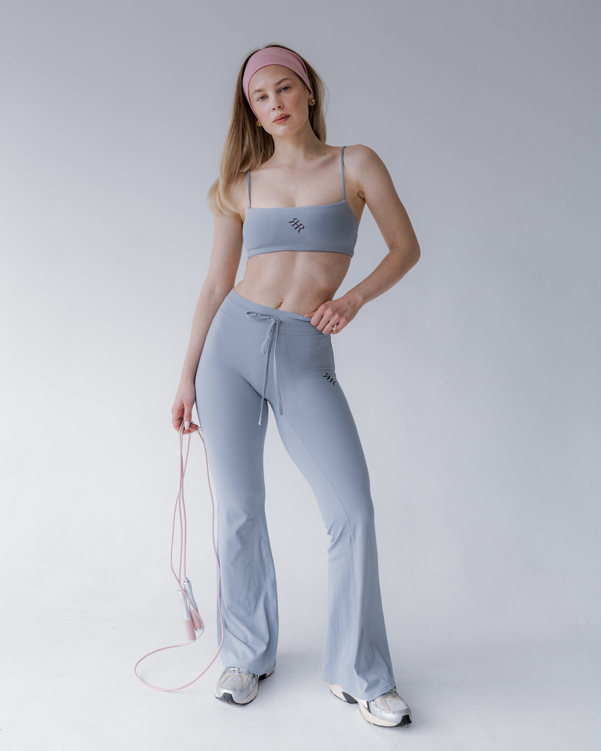 Woman in light gray athletic wear holding a jump rope on a white background