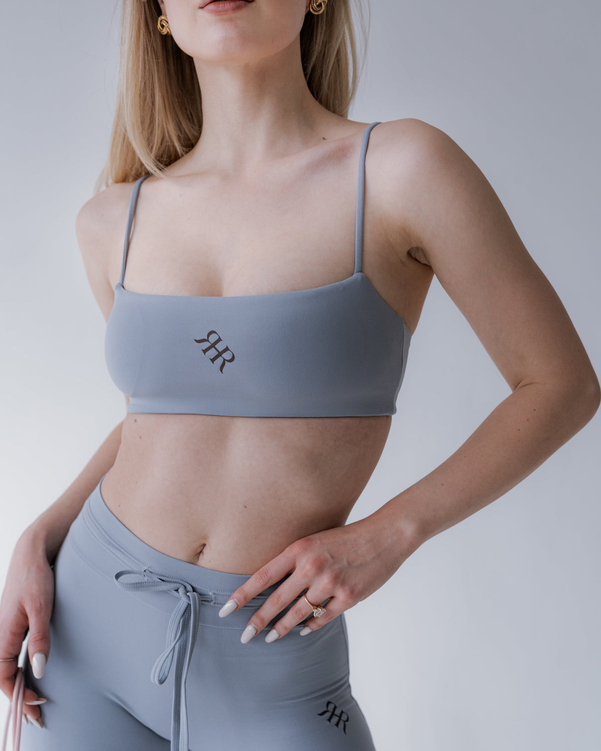 Woman wearing a gray sports bra and leggings with a logo on a plain background