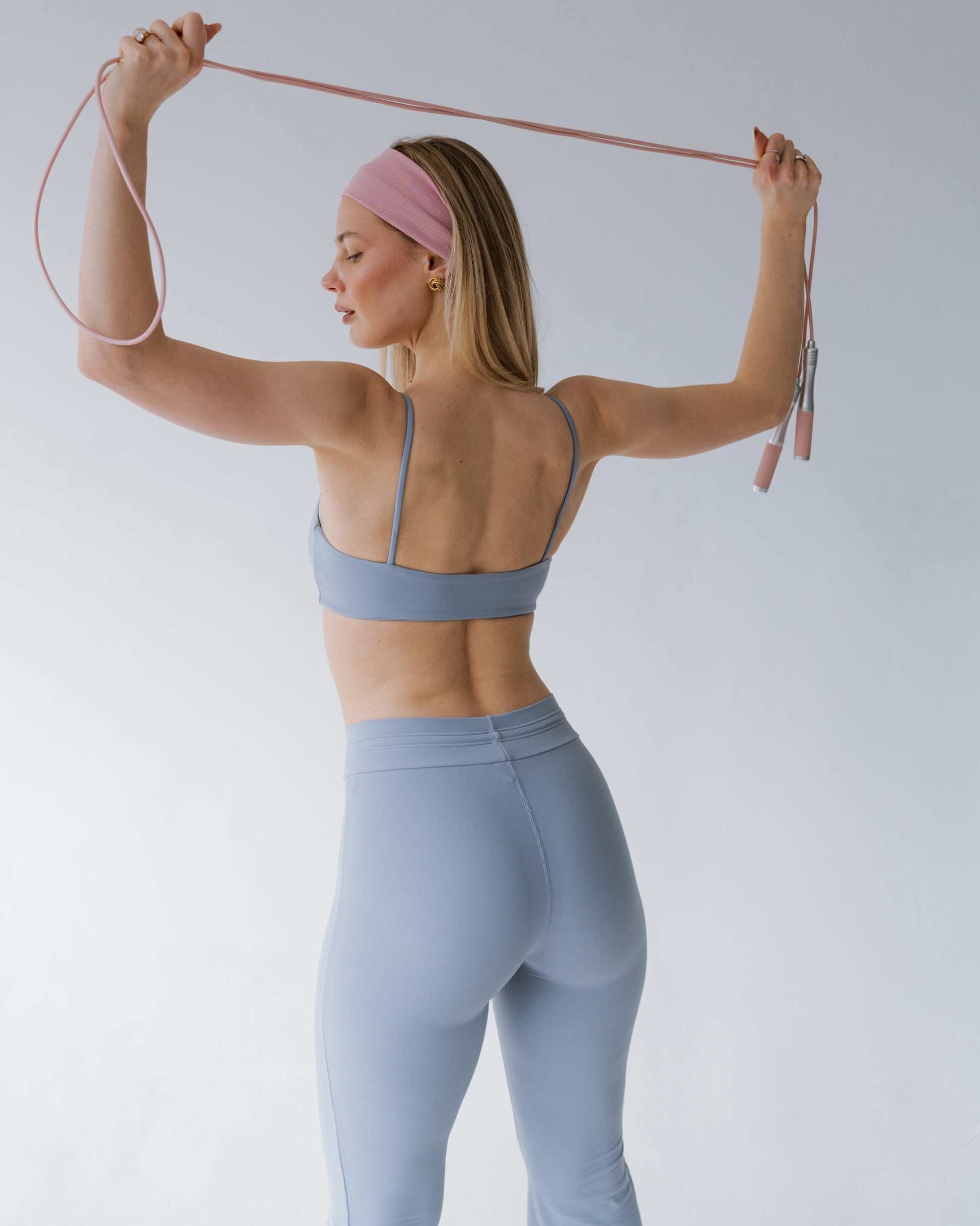 Woman in light blue athletic wear using resistance bands against a plain background