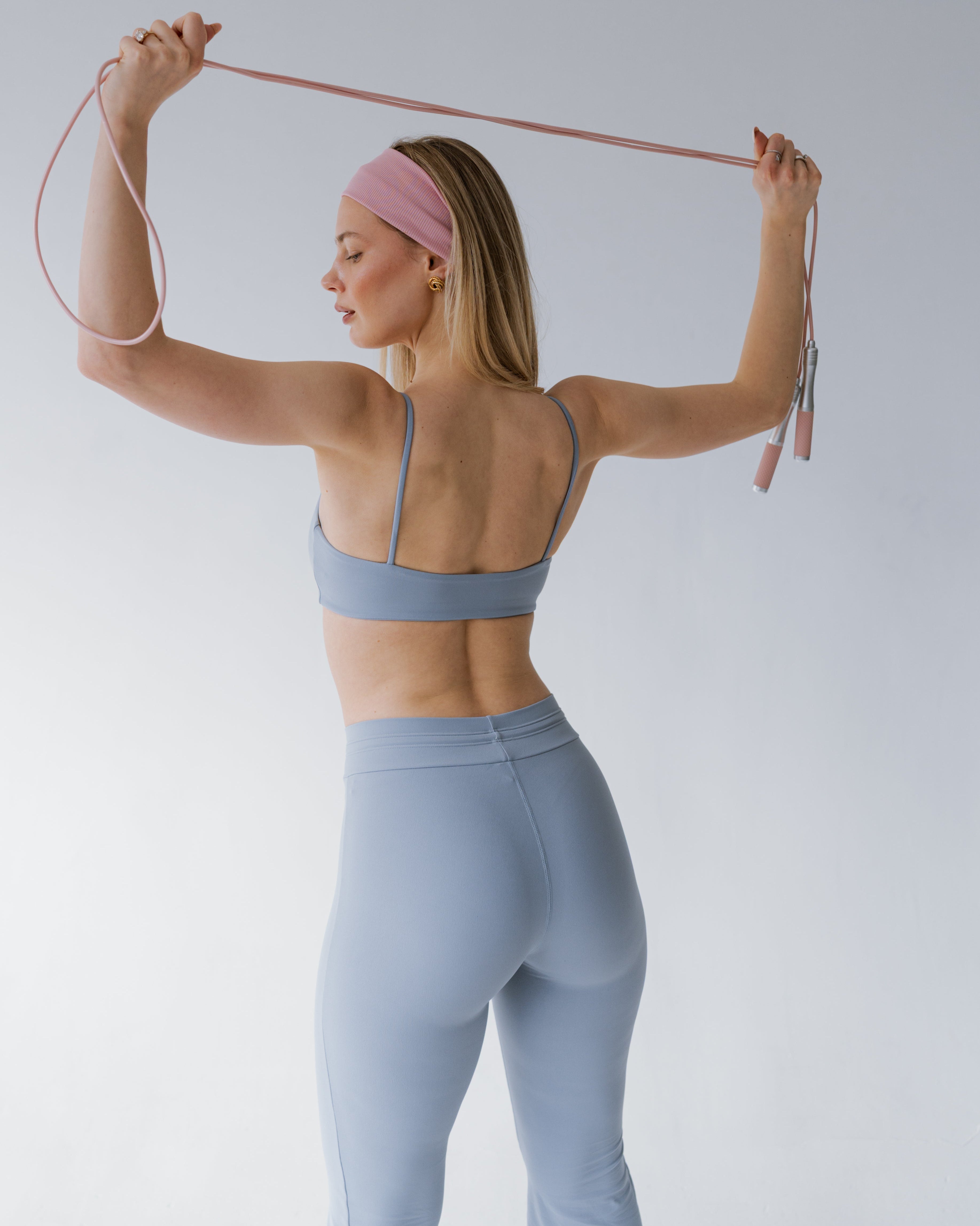 Woman in light blue athletic wear using resistance bands against a plain background