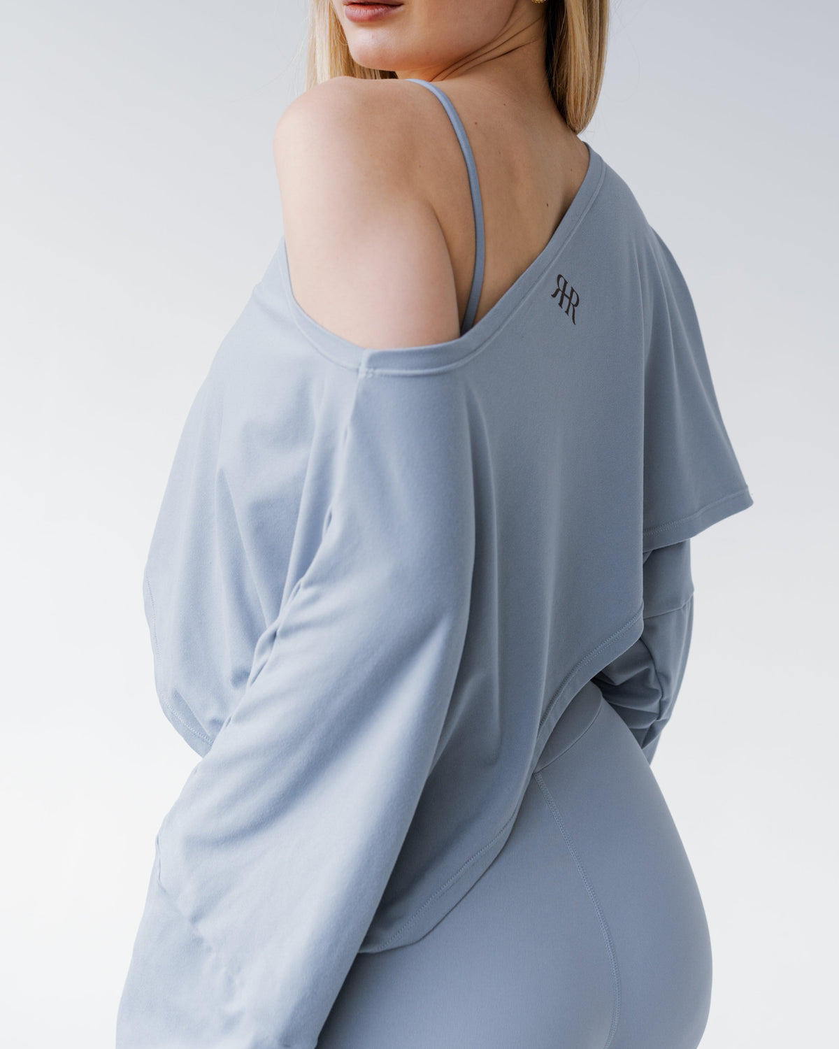 Woman wearing a light gray long-sleeve top with a brand logo on a white background