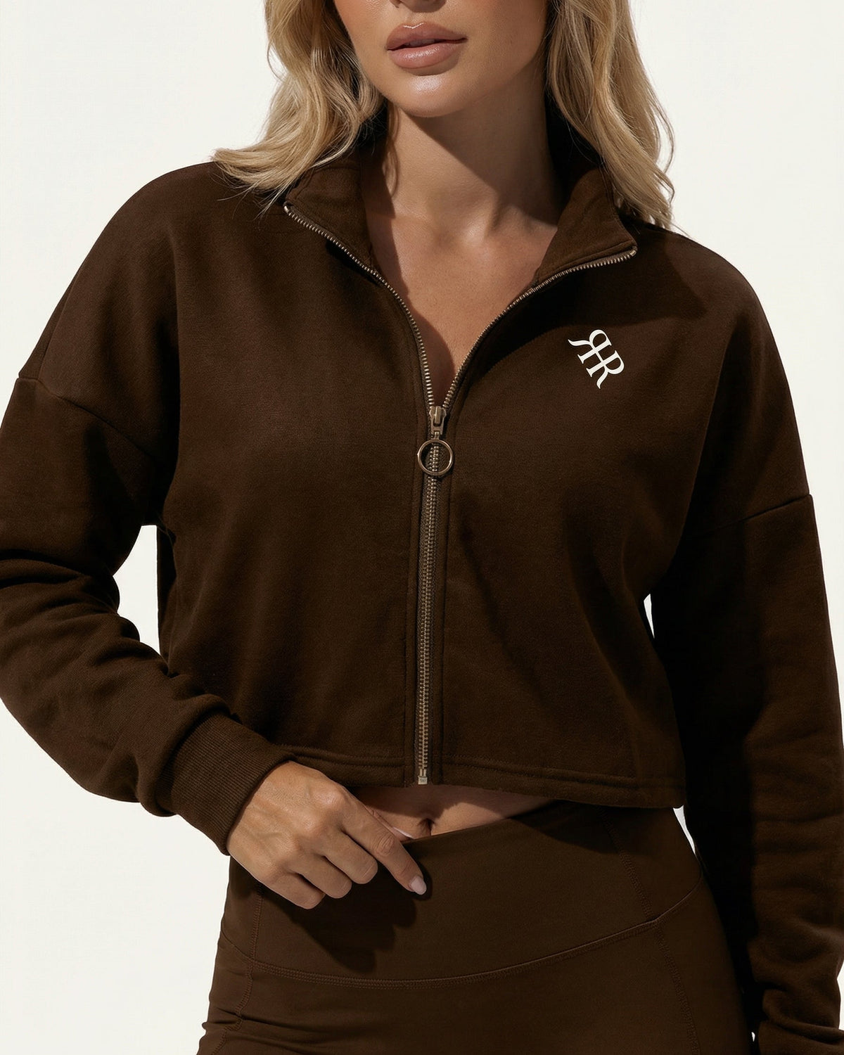Woman wearing a brown zip-up sweatshirt with a logo on a white background