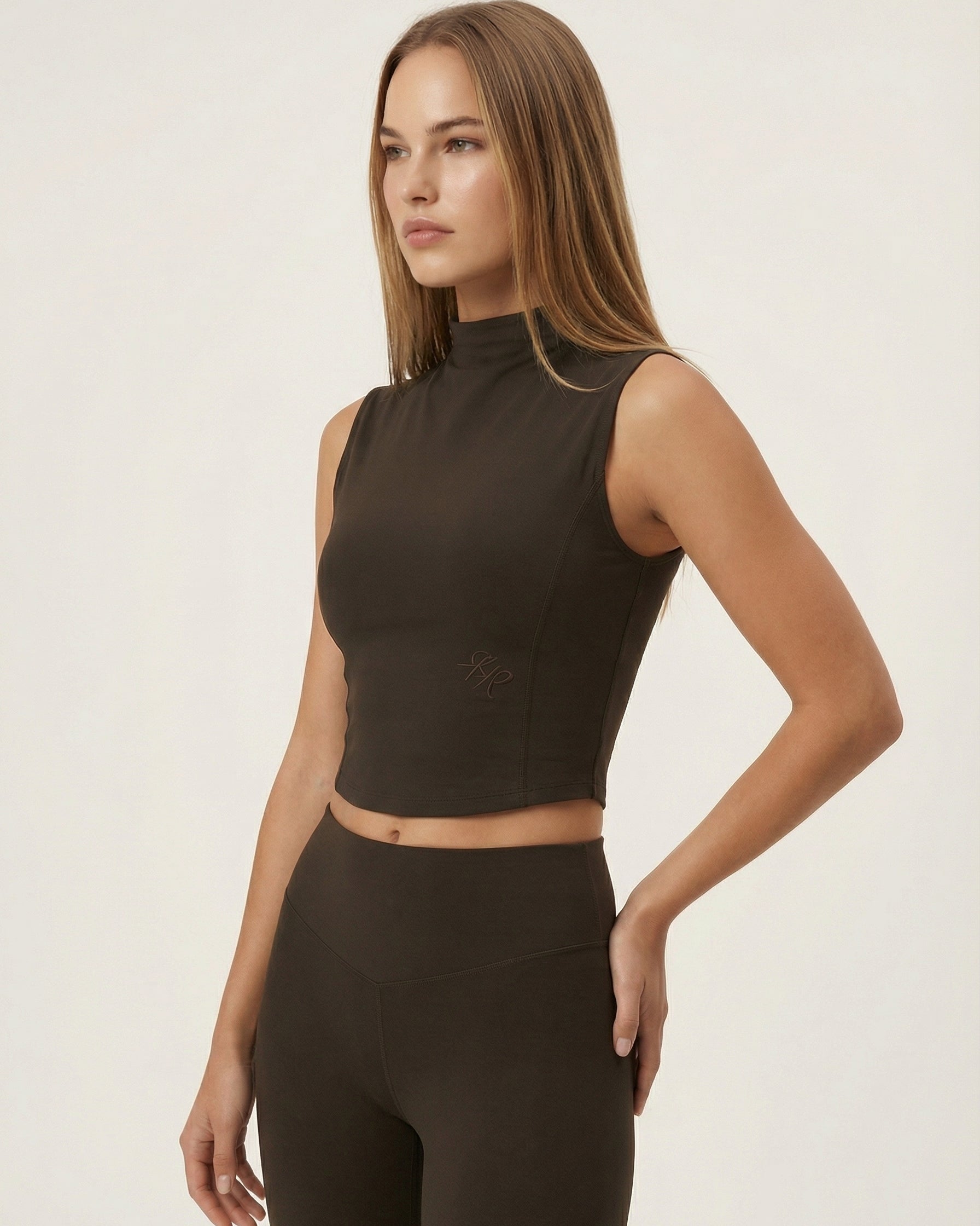 Woman wearing a brown sleeveless top and high-waisted leggings on a white background