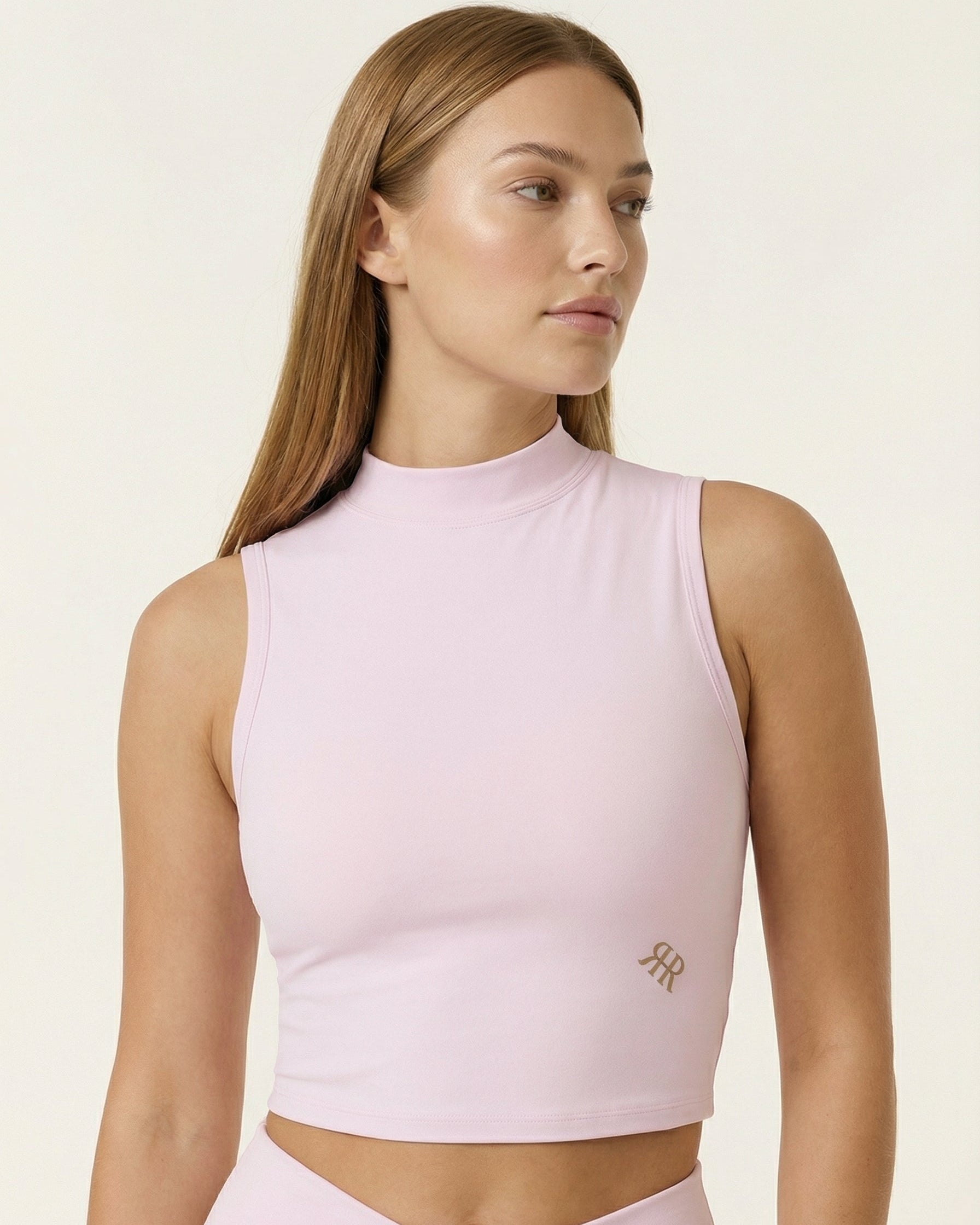 Woman wearing a light pink sleeveless top with a logo on a beige background
