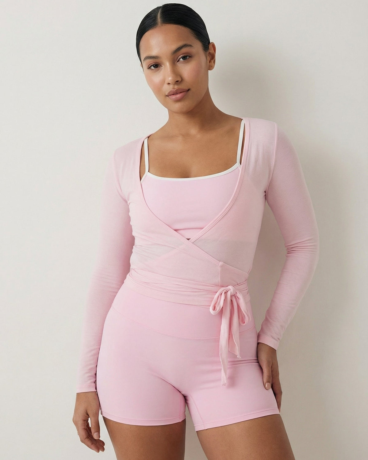 Woman wearing a pink long-sleeve top and shorts set against a plain background