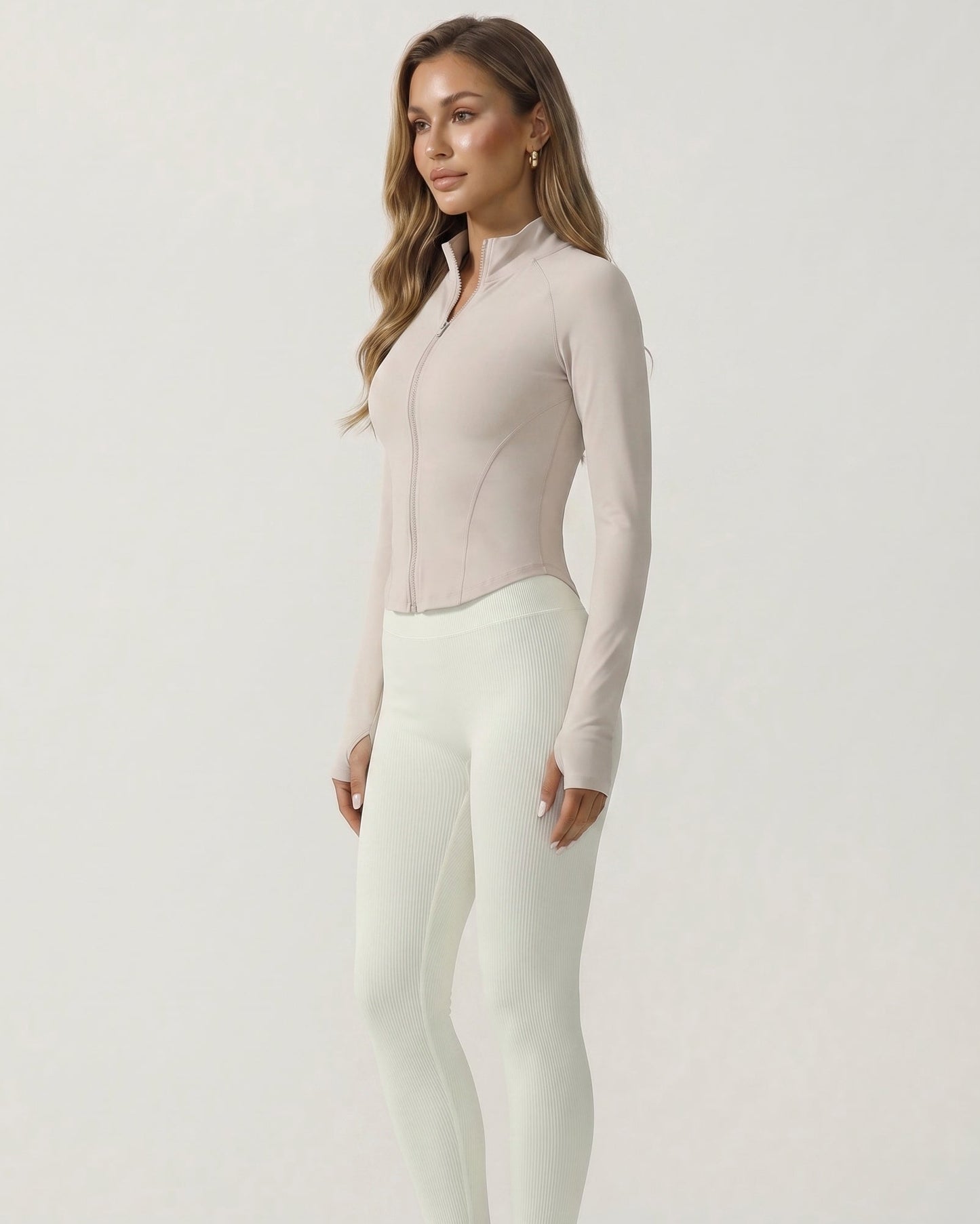 Woman wearing a beige long-sleeve top and white pants on a light gray background