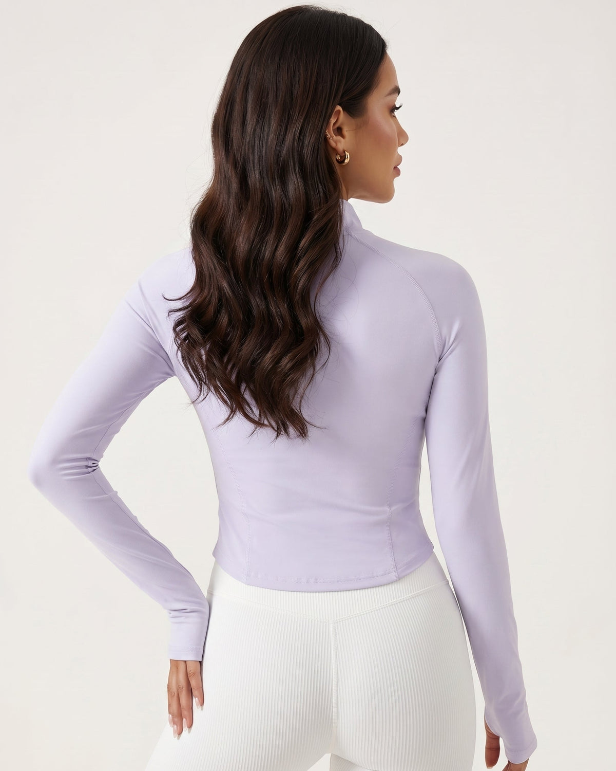 Woman wearing a light purple long-sleeve top and white pants on a plain background
