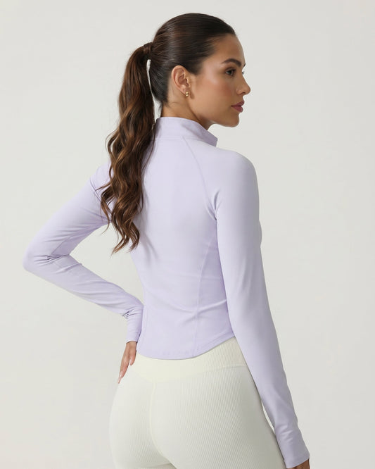 Woman wearing a light purple long-sleeve athletic top and white leggings on a plain background