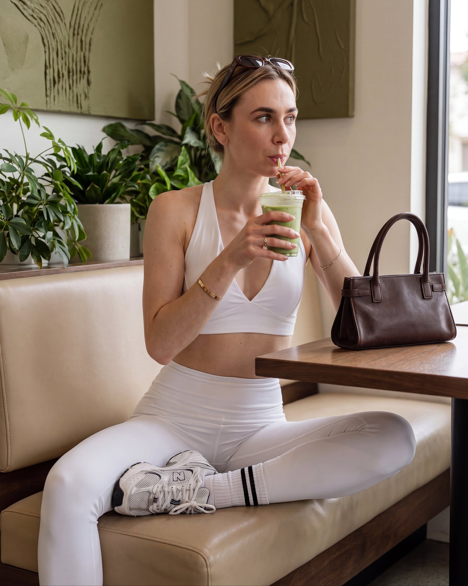 Woman in athletic wear drinking a green smoothie in a cafe.