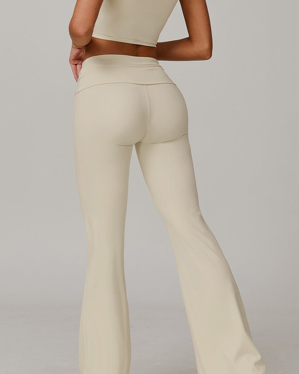 Person wearing a cream-colored outfit with flared pants on a plain background